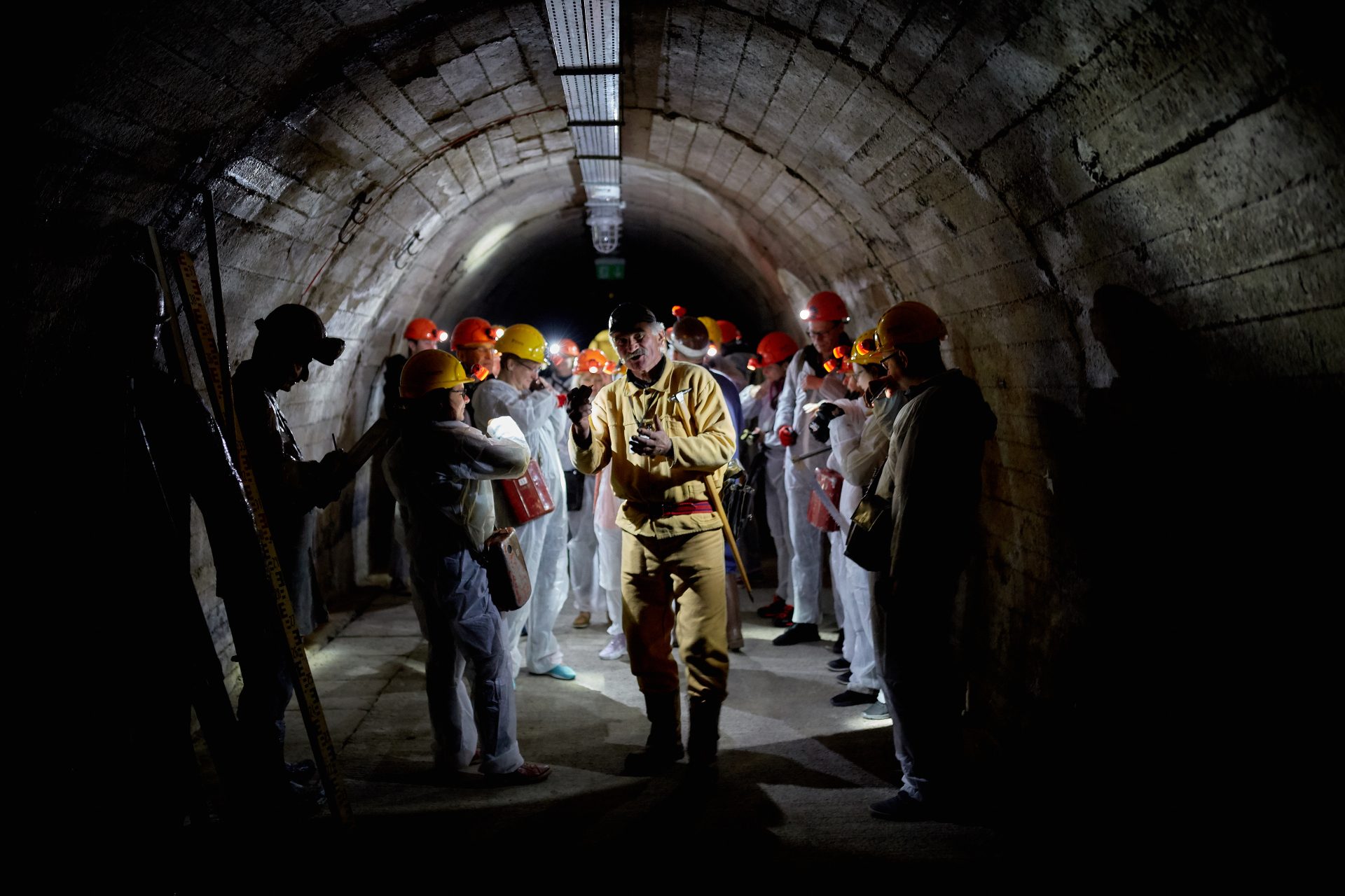 Grupa zwiedzających w czerwonych kaskach zwiedza podziemny tunel