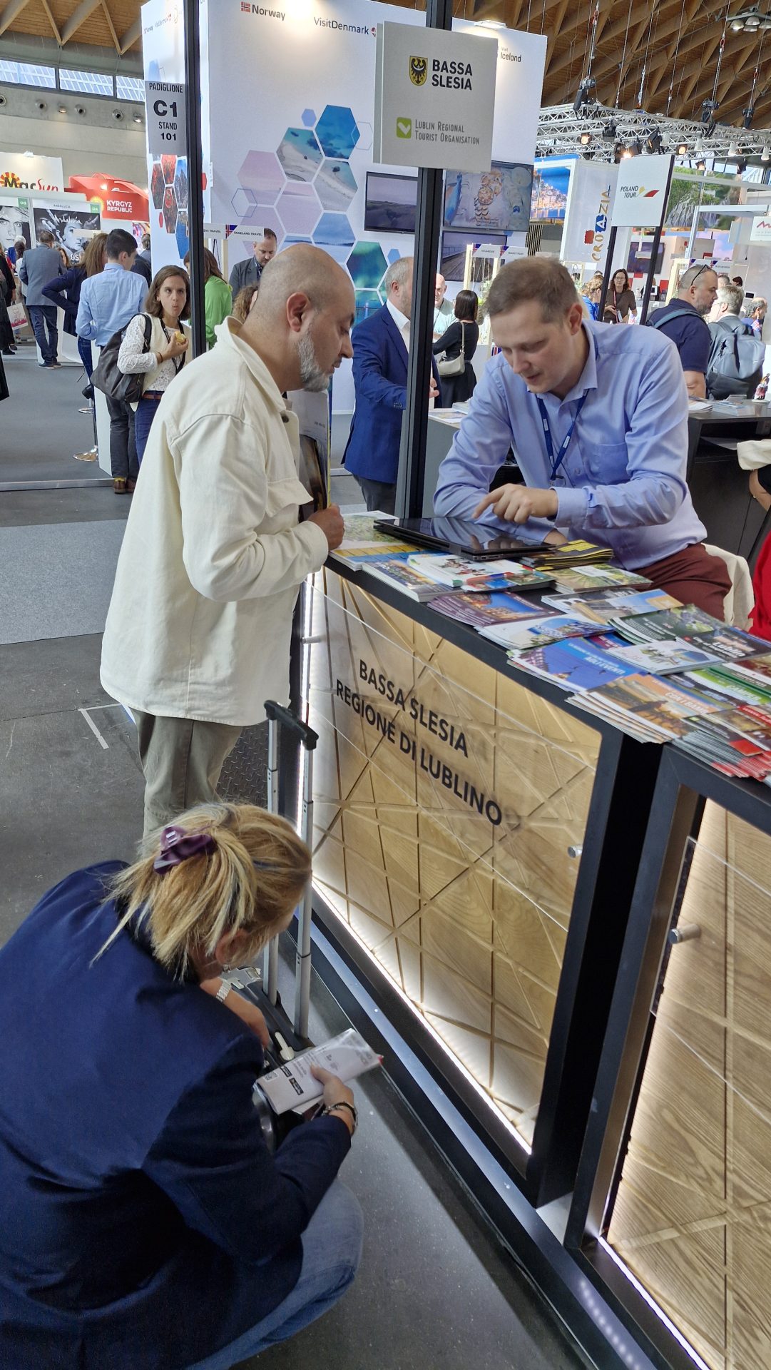 Zdjęcie stosika promocyjnego podczas targów turystycznych z mężczyzną pochylającym się nad ladą z drukami promocyjnymi