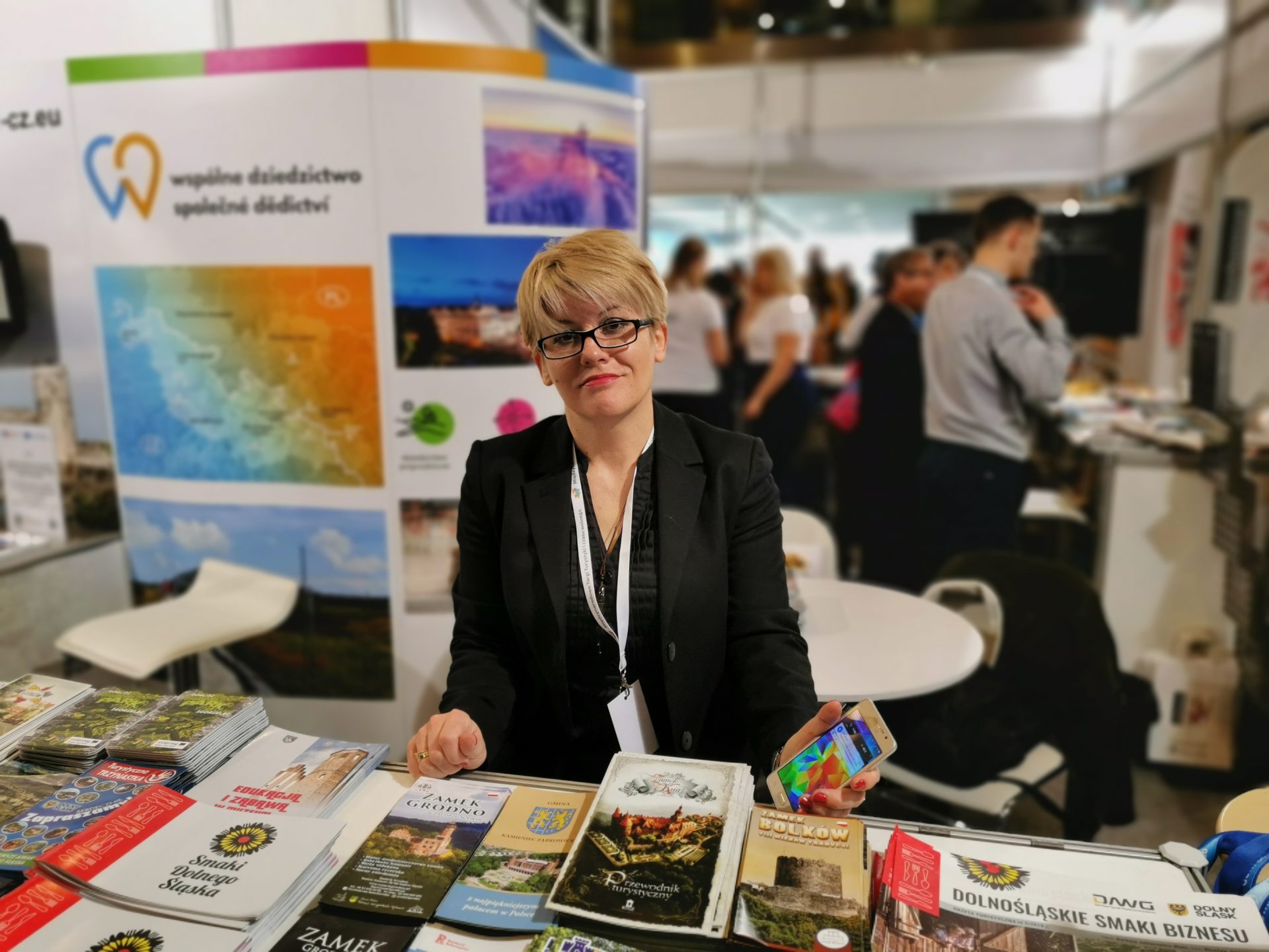 Zdjęcie uśmiechniętej kobiety na stoisku promocyjnym podczas targów turystycznych we Wrocławiu